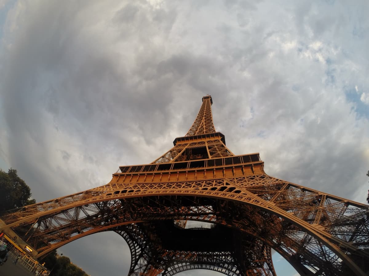 La Torre Eiffel fotografiada en contrapicado desde su base, con los cuatro pilares de hierro abriéndose sobre el objetivo y un cielo nublado de fondo.